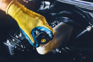Image of a hand wearing a blue and yellow glove unscrewing the cap on the brake fluid hose to represent changing brake fluid.