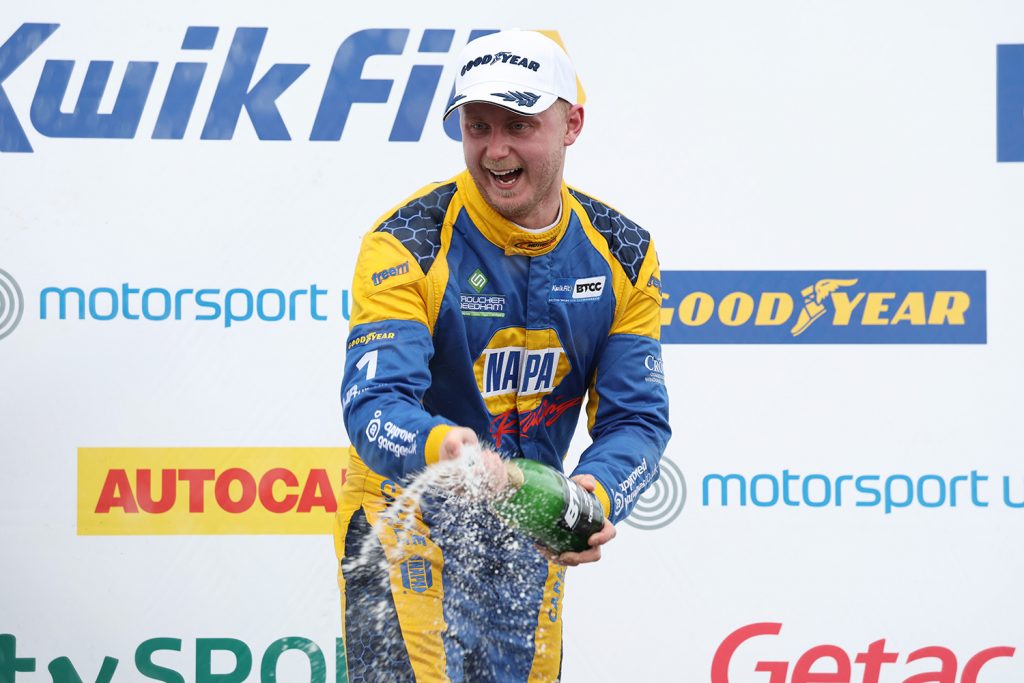NAPA Racing UK's Ash Sutton celebrates his BTCC Knockhill P1 victory with a bottle of champagne on the podium.