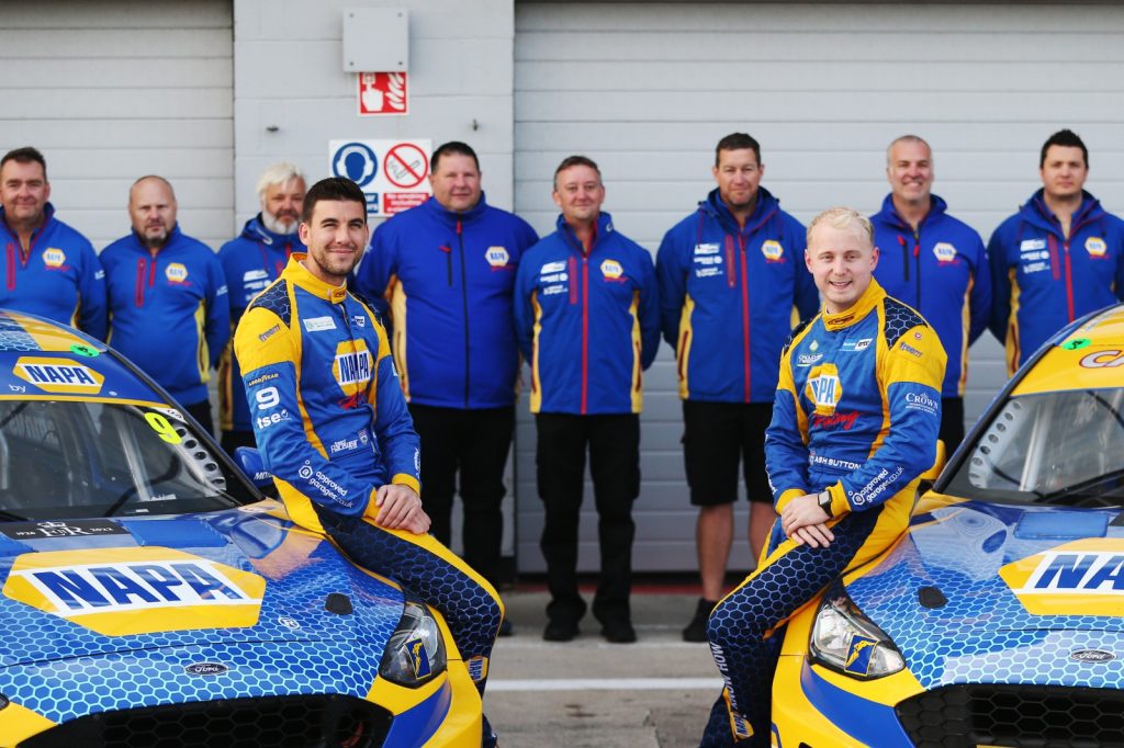 NAPA Racing UK's Dan Cammish and Ash Sutton lean on their NAPA Ford Focus STs with their team lined up behind them wearing NAPA merch.