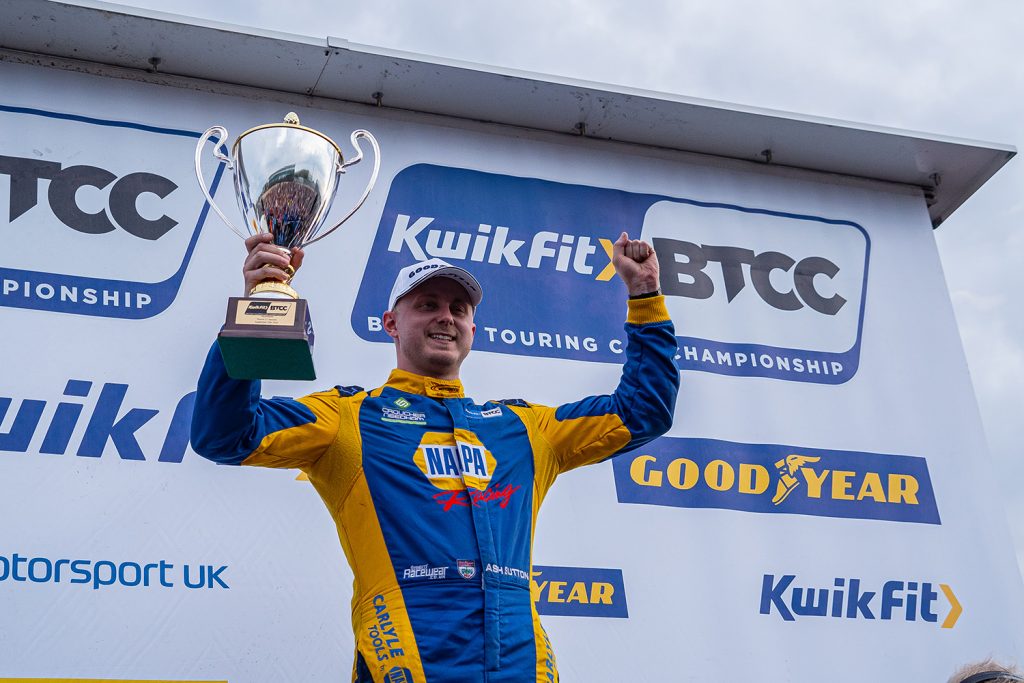 NAPA Racing UK's Ash Sutton celebrates victory on the podium with trophy in the air