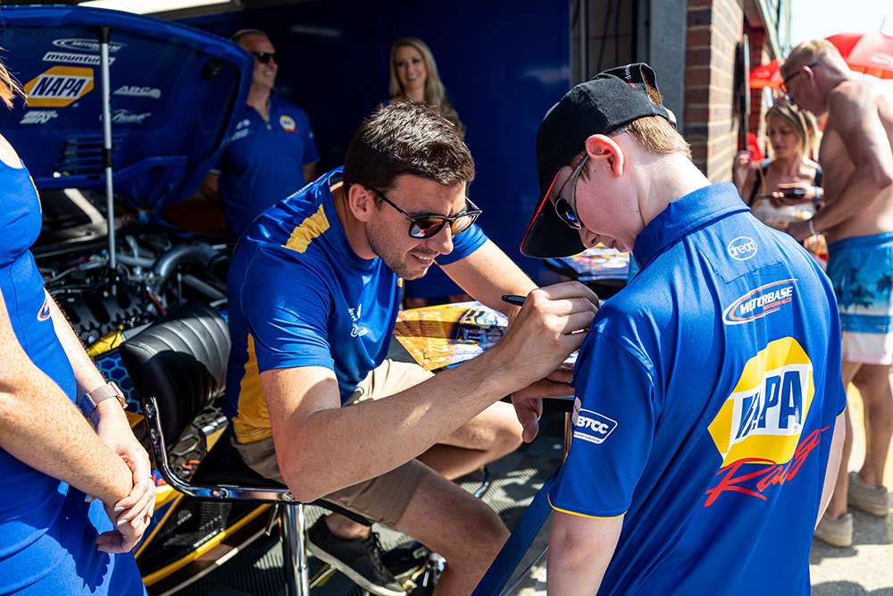 Dan Cammish signs his name on a NAPA Racing UK shirt worn by a young fan.